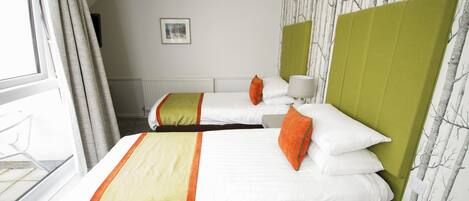 A hotel room with two beds, each with white bedding and orange pillows, green headboards, and a window with curtains.