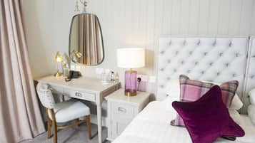 A hotel room with a bed, a desk, a chair, a vanity with a mirror, a lamp, and a bedside table.