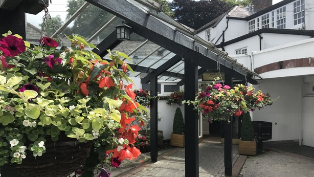 A covered outdoor area with hanging flower baskets and a brick pathway. - Crown Hotel (Carlisle)