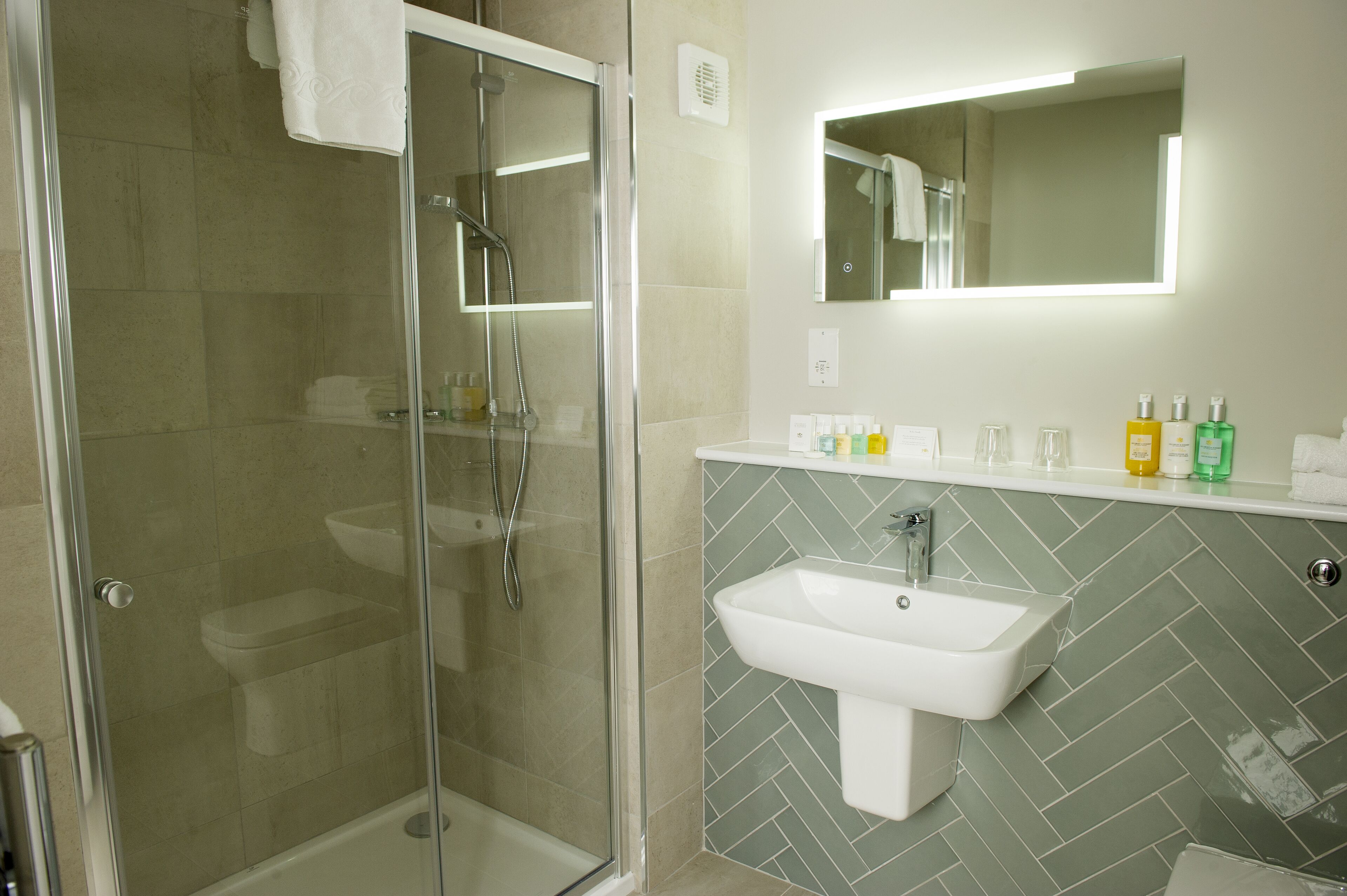A modern bathroom with a glass-enclosed shower, a white sink, and a herringbone-patterned backsplash.