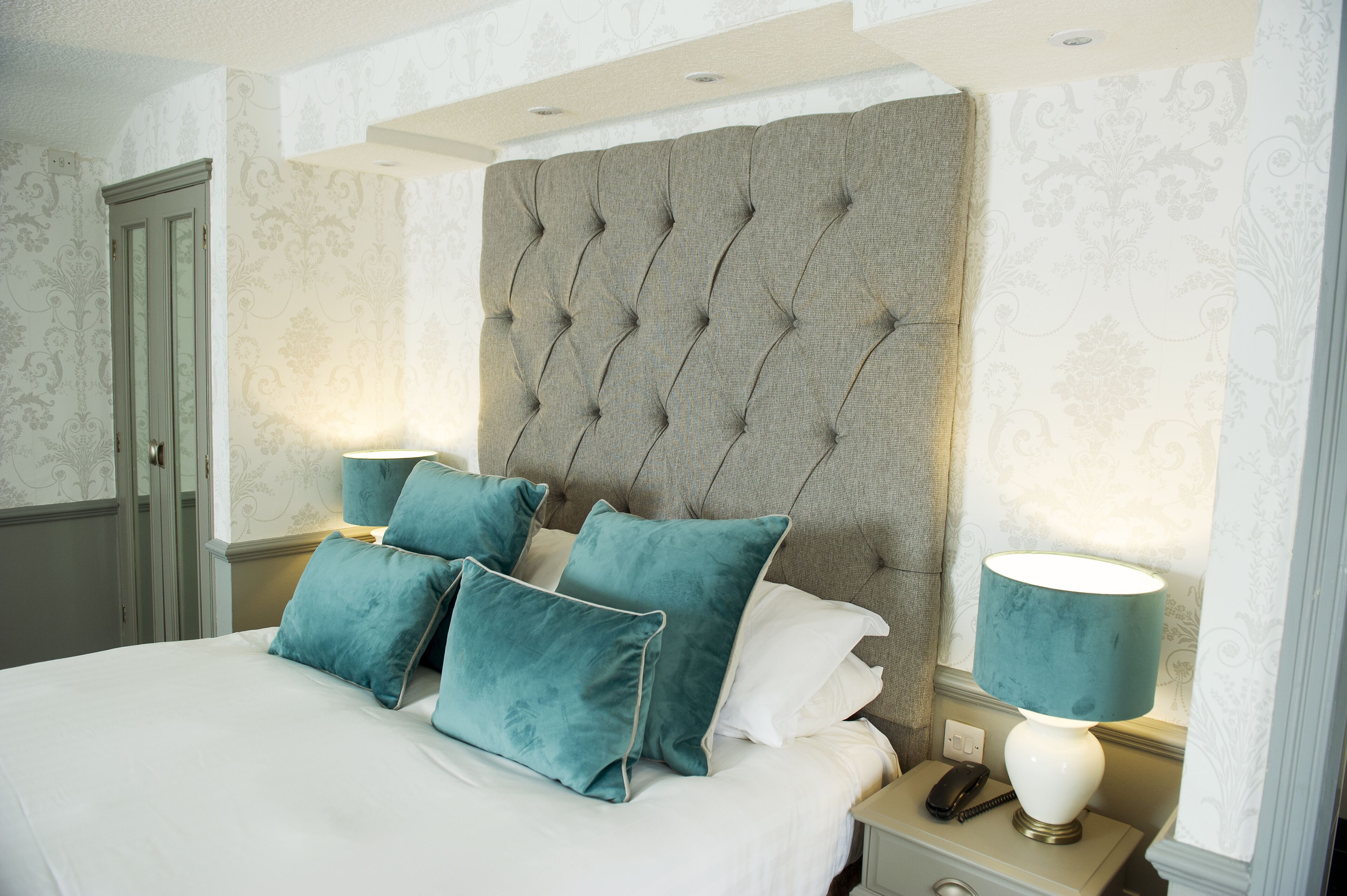 A neatly made bed with teal and white pillows, a tufted headboard, and a bedside lamp.