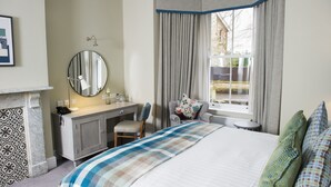 A hotel room with a bed, a desk with a chair, a round mirror, a small table, and a window with curtains. - Crown Hotel (Carlisle)