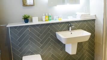 A bathroom with a white toilet, a sink, a mirror, and a herringbone-patterned backsplash.