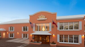 Un hôtel à la façade de couleur pêche, avec une enseigne bien visible indiquant « INVERIE EXECUTIVE SUITES », et deux drapeaux de chaque côté de l’entrée.
