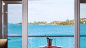 Un balcon avec une table et des chaises, un saladier en verre, et une vue sur la mer et le littoral au loin.