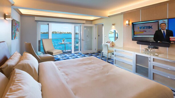 Une chambre d’hôtel avec un grand lit, un bureau, une télévision et une vue sur la mer.