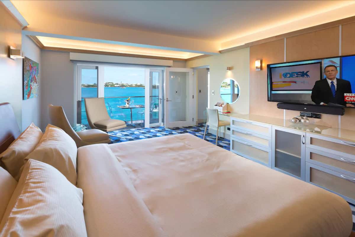 A hotel room with a large bed, a desk, a television, and a view of the sea.