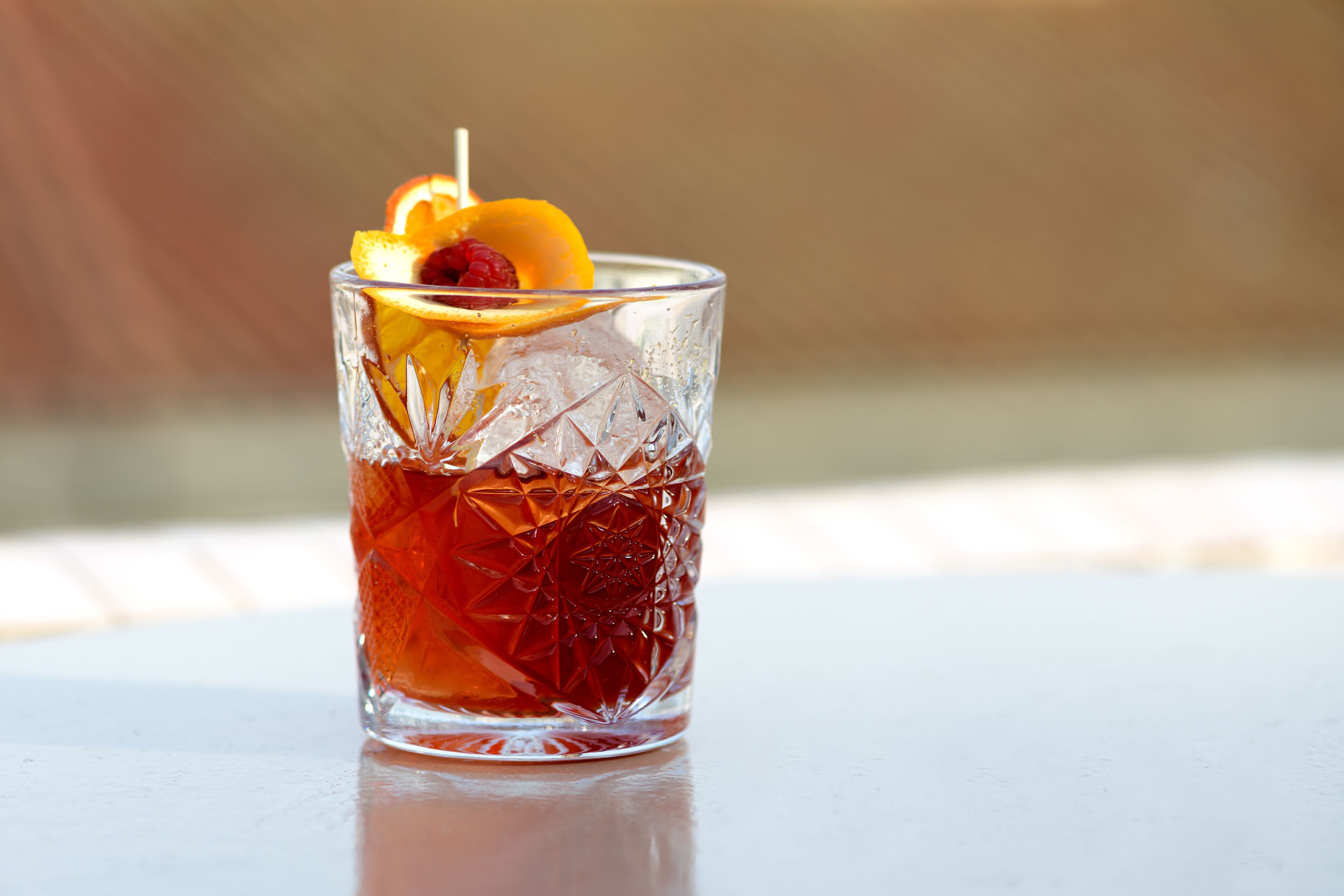 Un vaso transparente con un diseño texturizado, lleno de una bebida roja, adornado con una rodaja de naranja y una baya.