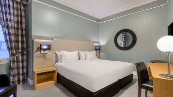 Una habitación de hotel con una cama grande, mesitas de noche, un escritorio y una silla.