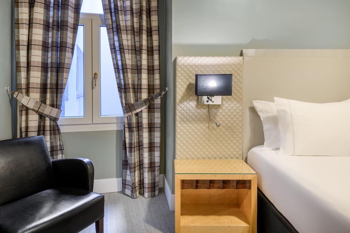 A hotel room with a bed, a TV on a wall, a chair, and plaid curtains.