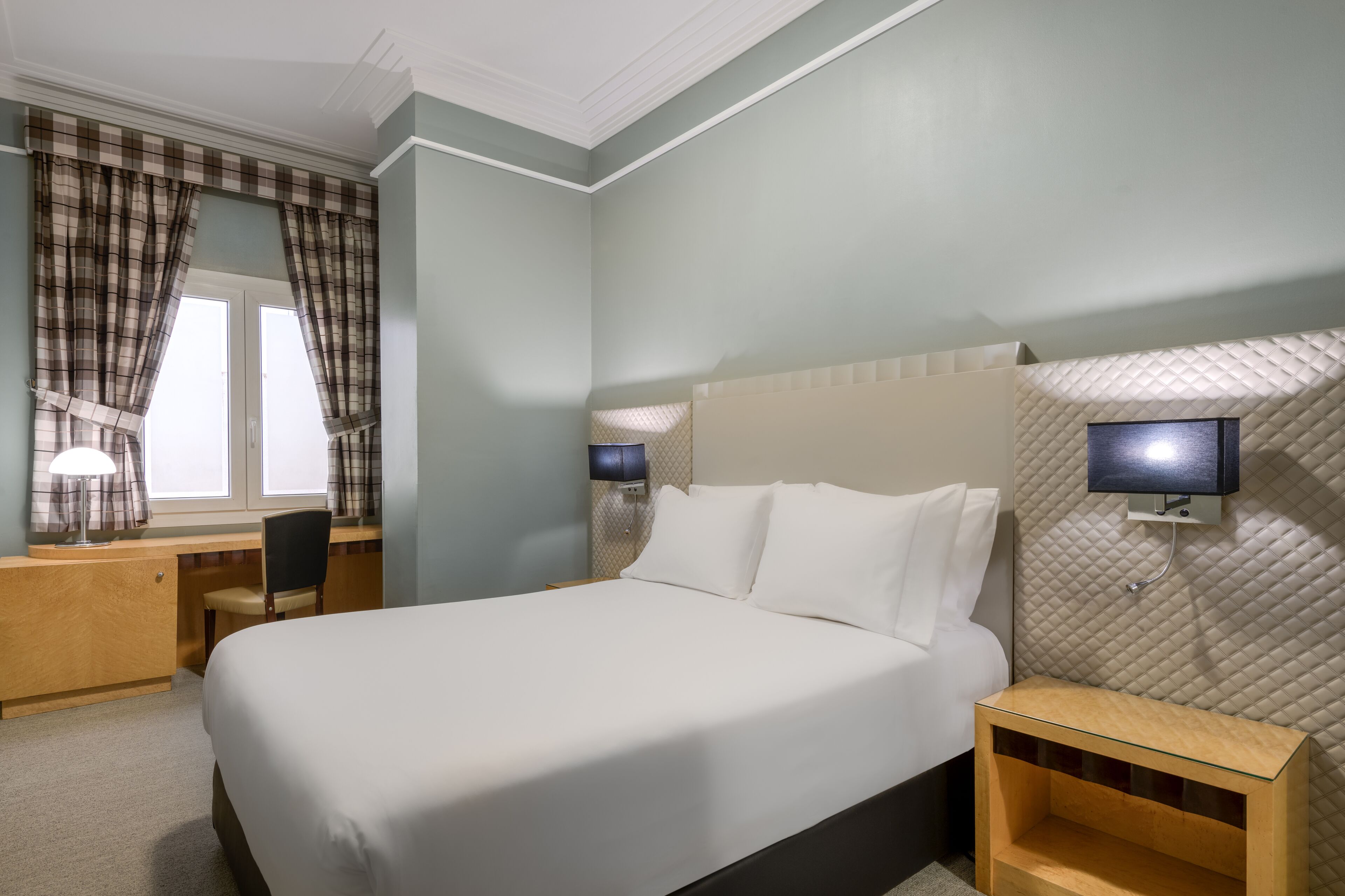 Habitación de hotel con cama, escritorio, silla y dos lámparas de noche.
