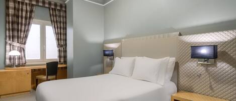 Habitación de hotel con cama, escritorio, silla y dos lámparas de noche.
