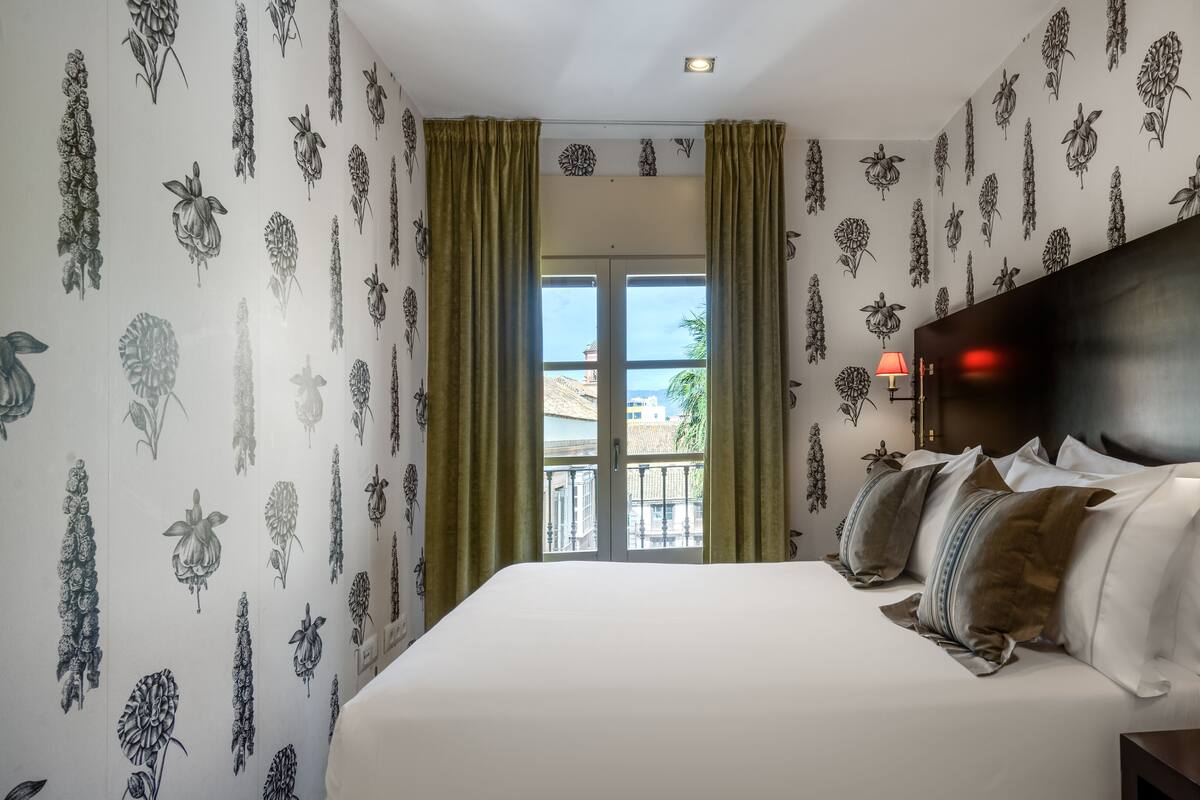 A bedroom with a large bed, green curtains, and floral wallpaper.