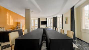 A conference room with a long table, chairs, a flat-screen TV, and a buffet area with food and drinks.