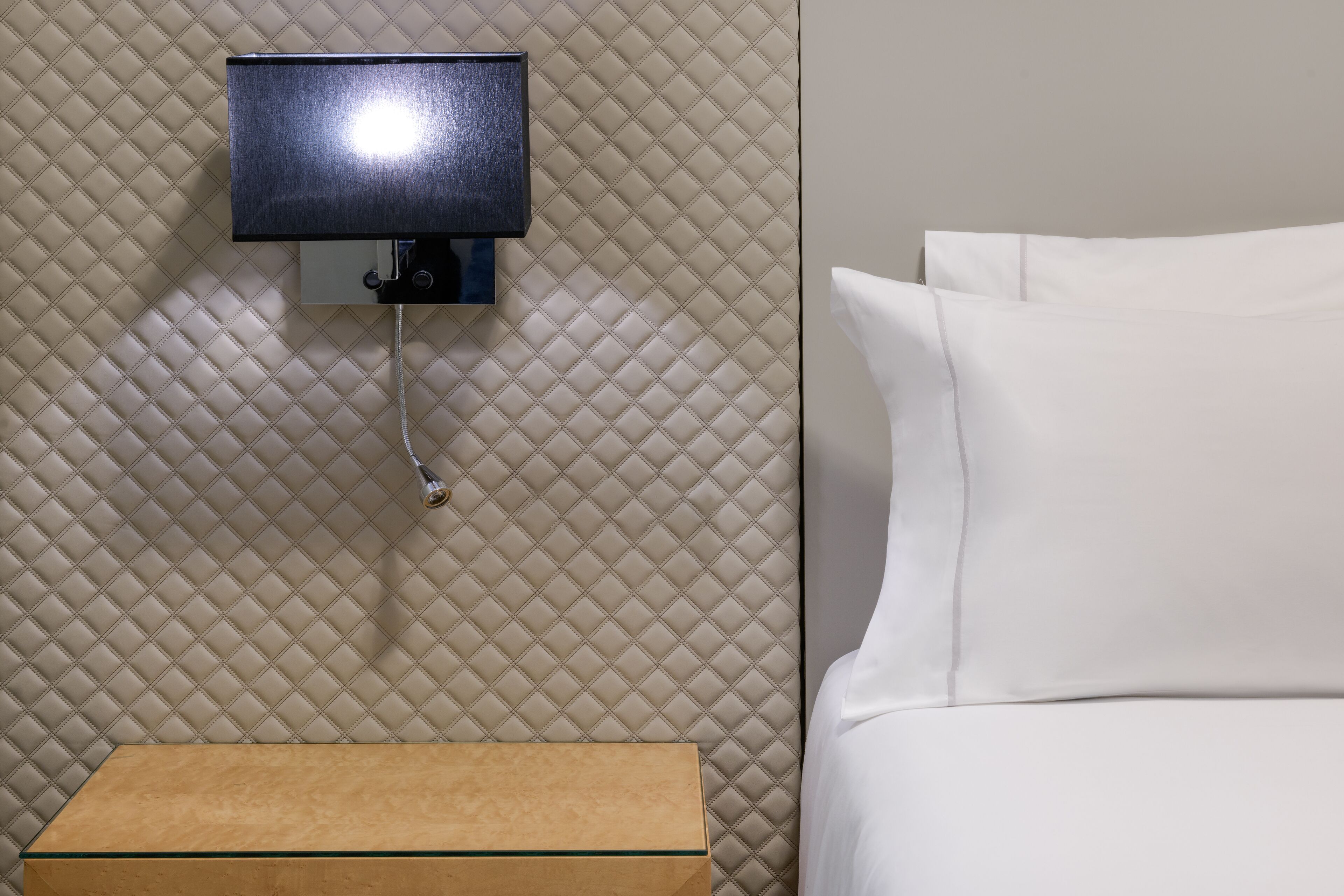 Una habitación de hotel con una cama, una mesita de noche y un televisor instalado en la pared.