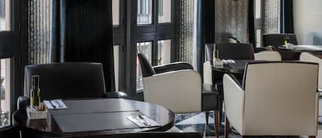 Un restaurante con piso a cuadros, sillas negras y blancas y vistas a edificios a través de amplios ventanales.