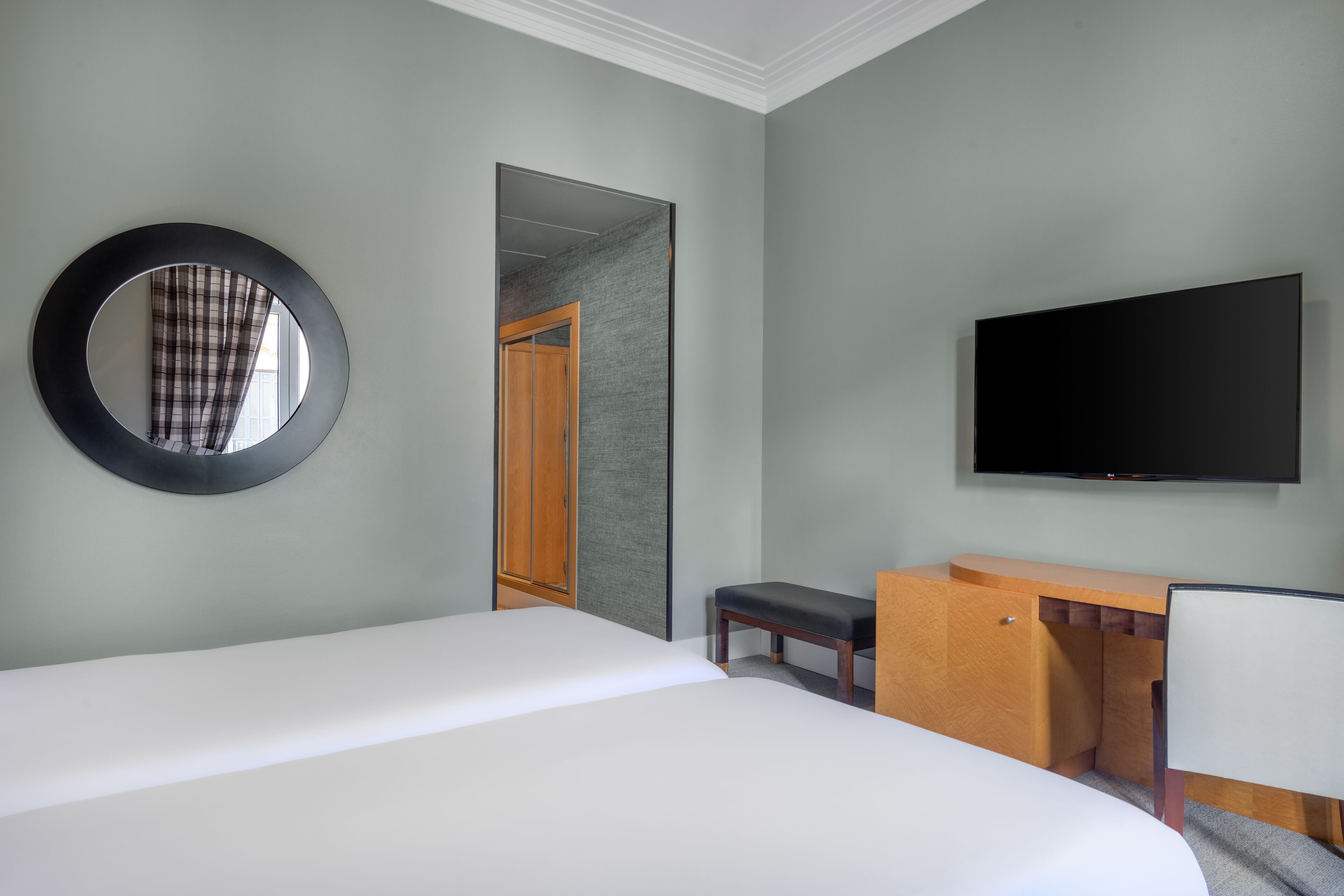 A hotel room with a bed, a desk, a chair, a television, and a mirror.