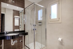 Un baño moderno con ducha de vidrio, lavamanos negro y un espejo grande.