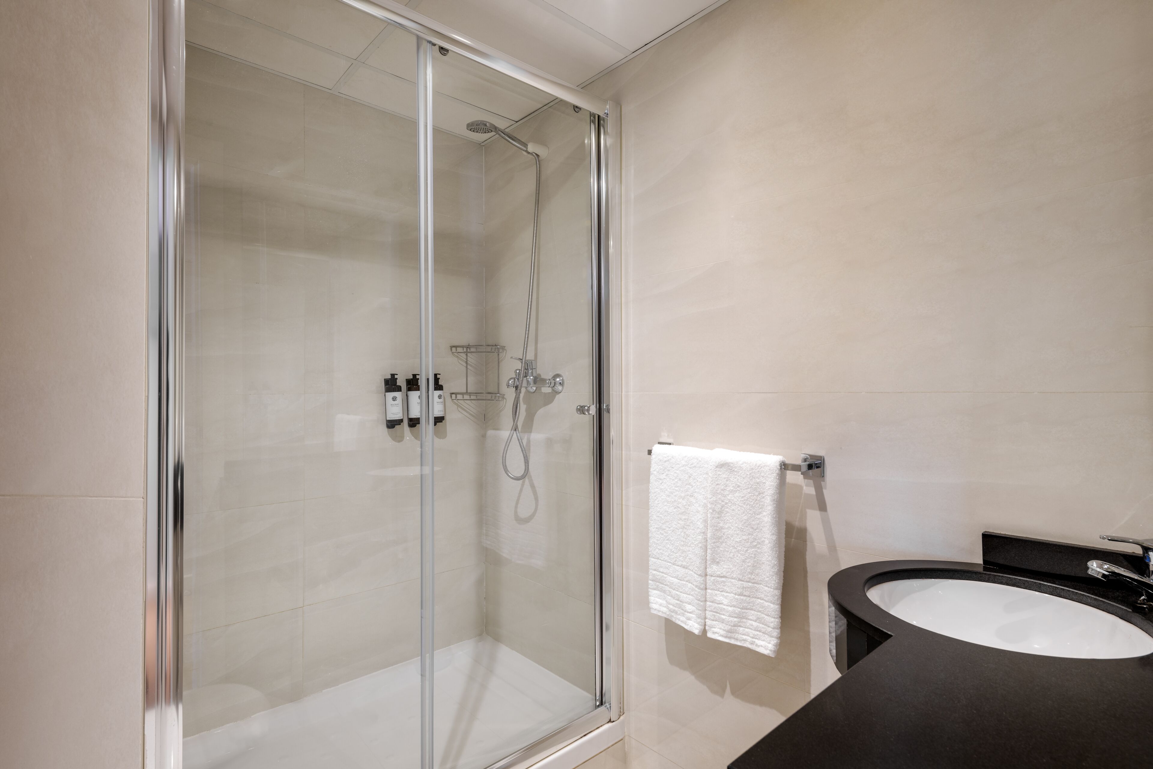 A modern bathroom with a glass-enclosed shower, a black sink, and a white towel hanging on the wall.