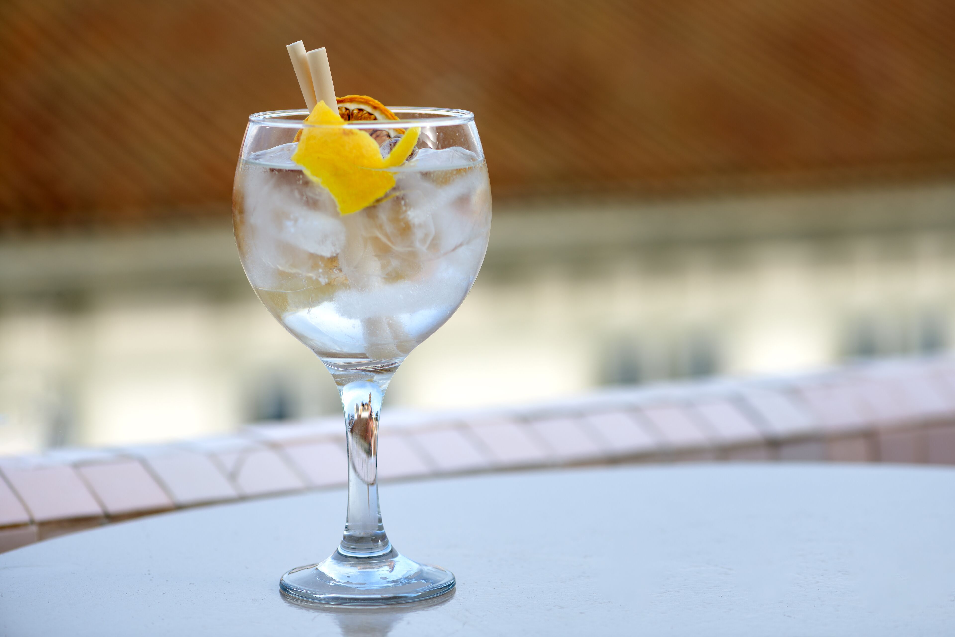 A clear glass with ice and a lemon slice garnish on a table with a tiled edge.