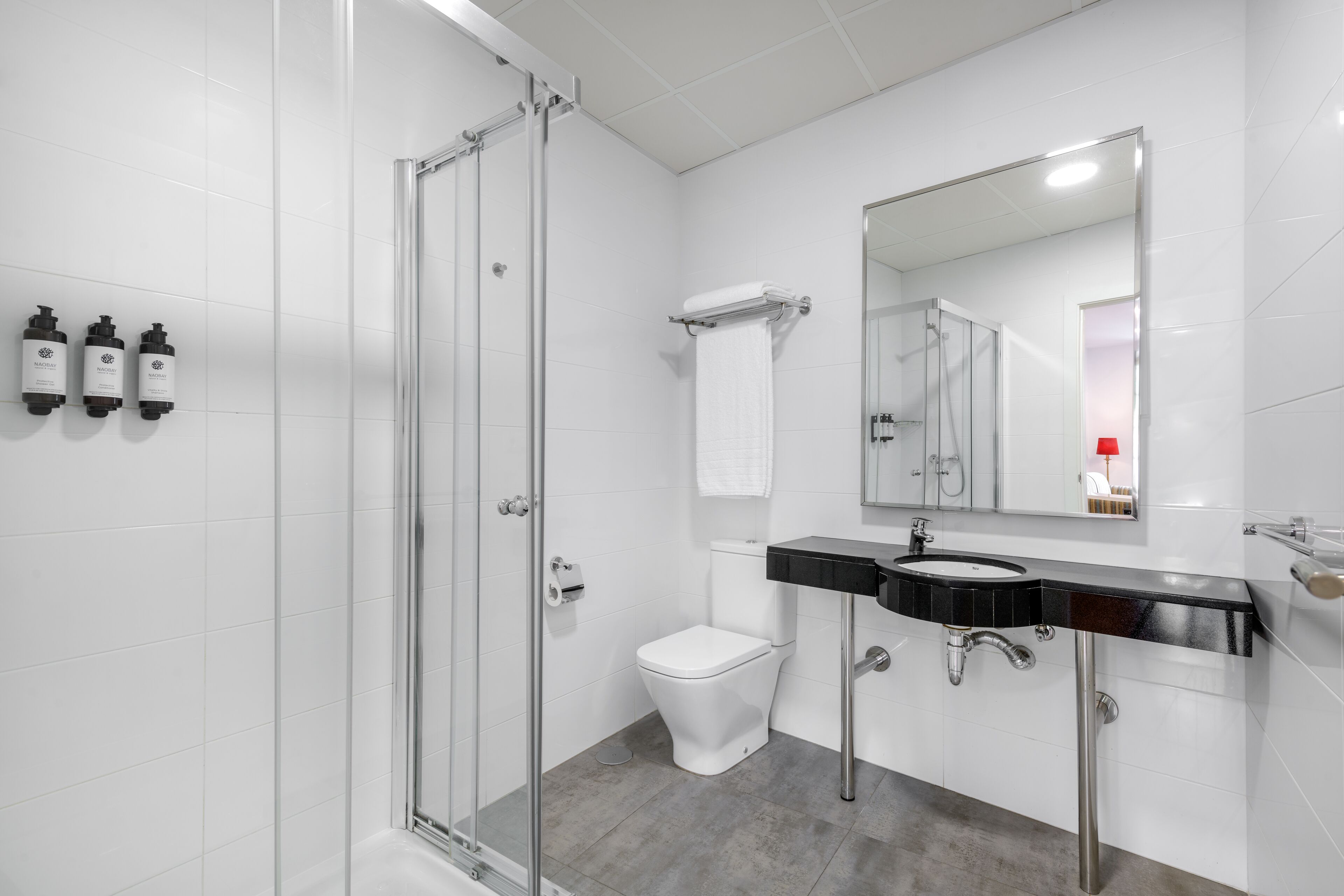 A modern bathroom with a glass shower enclosure, a white toilet, a black sink with a mirror above, and toiletries on the wall.