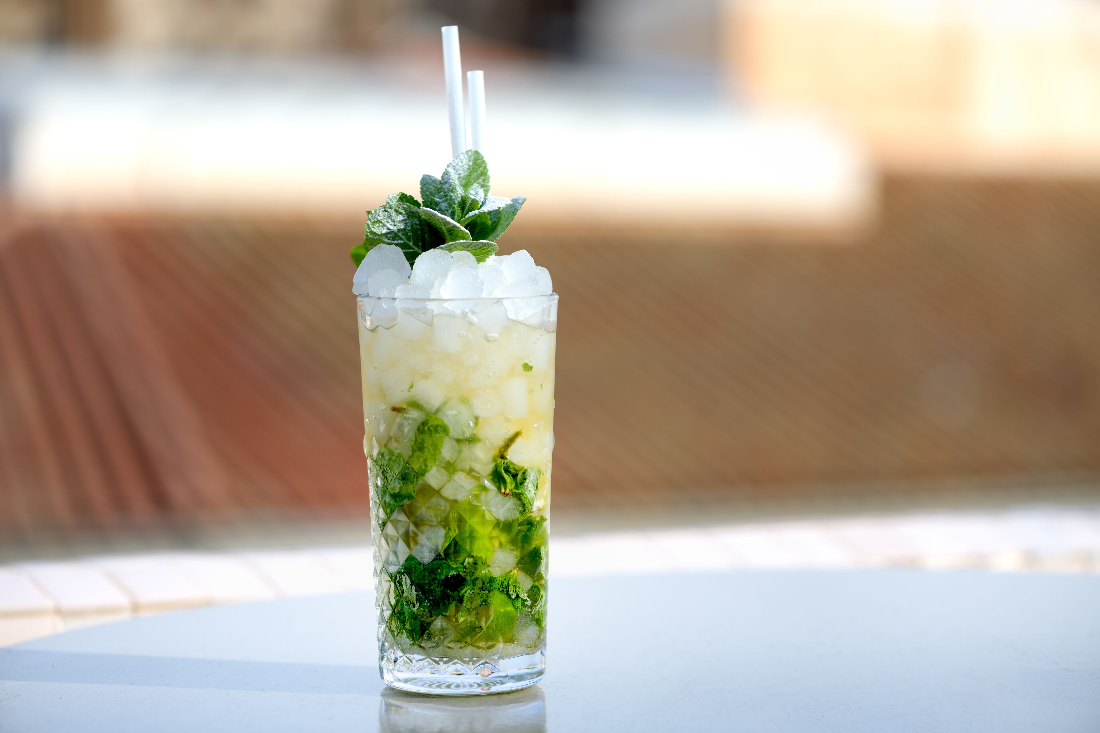 Un vaso alto con cubitos de hielo, hojas de menta y una pajita sobre una mesa.