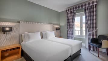 A double bed with white linens, a nightstand, a wall-mounted TV, and a window with plaid curtains.