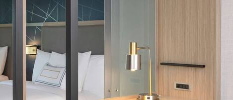 A modern hotel room with a glass partition separating the bed and desk area.