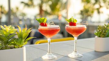 Two cocktails on a table with potted plants around.