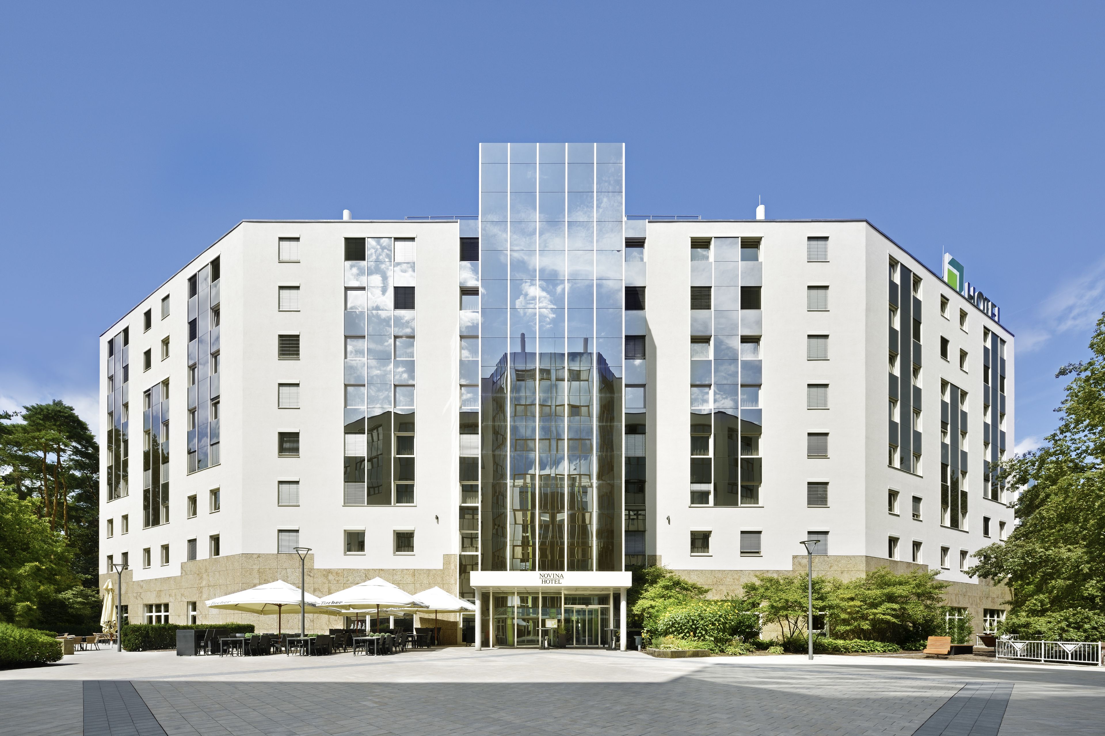A modern hotel with a central glass facade, multiple floors, and outdoor seating areas.