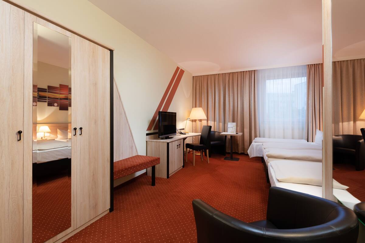Hotelkamer met een bed, bureau met een computer, stoel, televisie en raam met gordijnen.