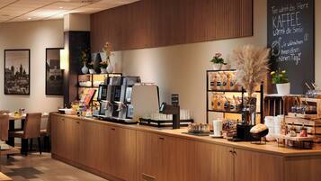 A coffee shop counter with a coffee machine, a menu board, and various coffee beans and pastries.