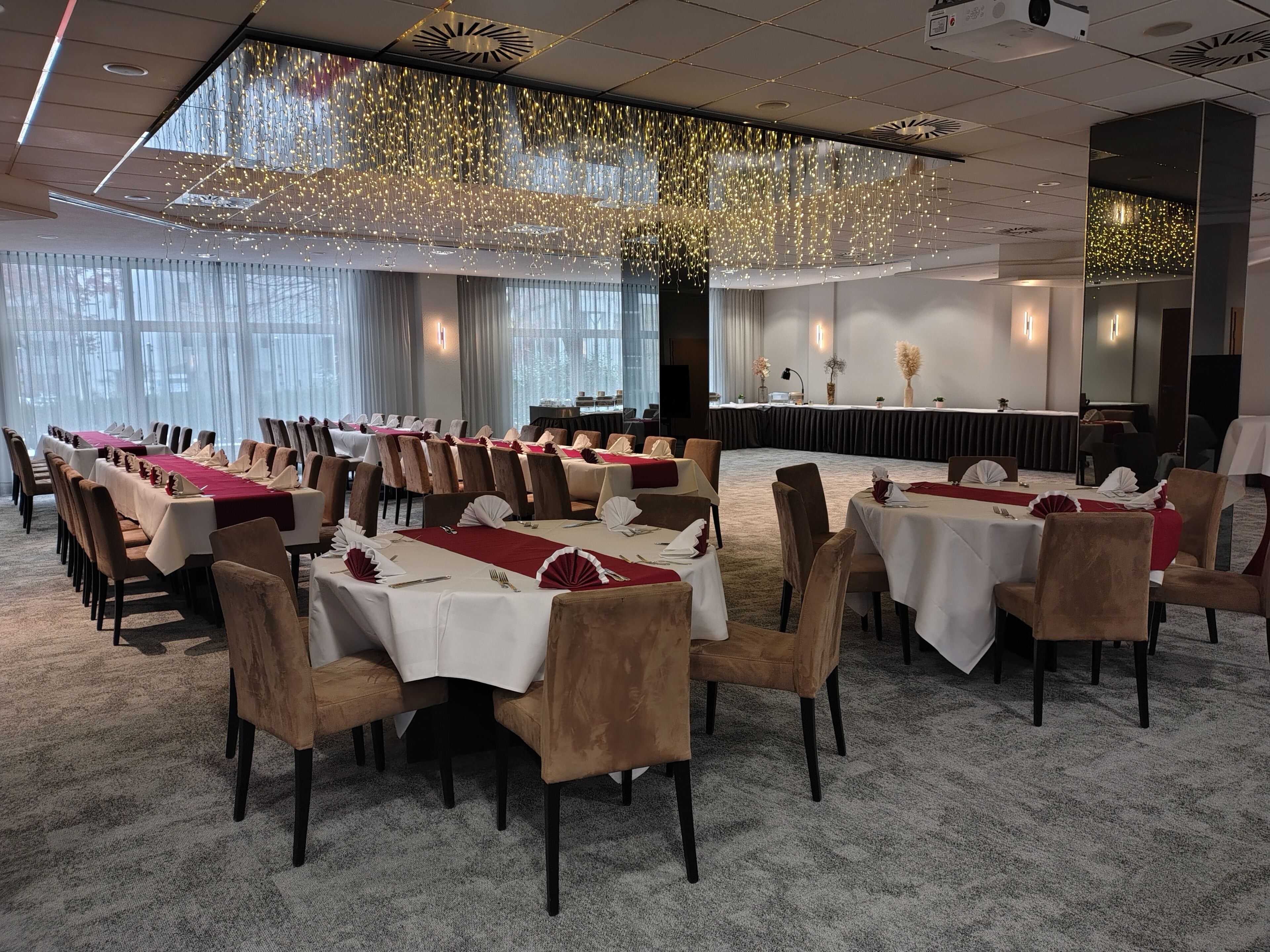 Une salle de conférence avec des tables disposées pour une réunion, une scène avec un pupitre et une grande fenêtre avec des rideaux.