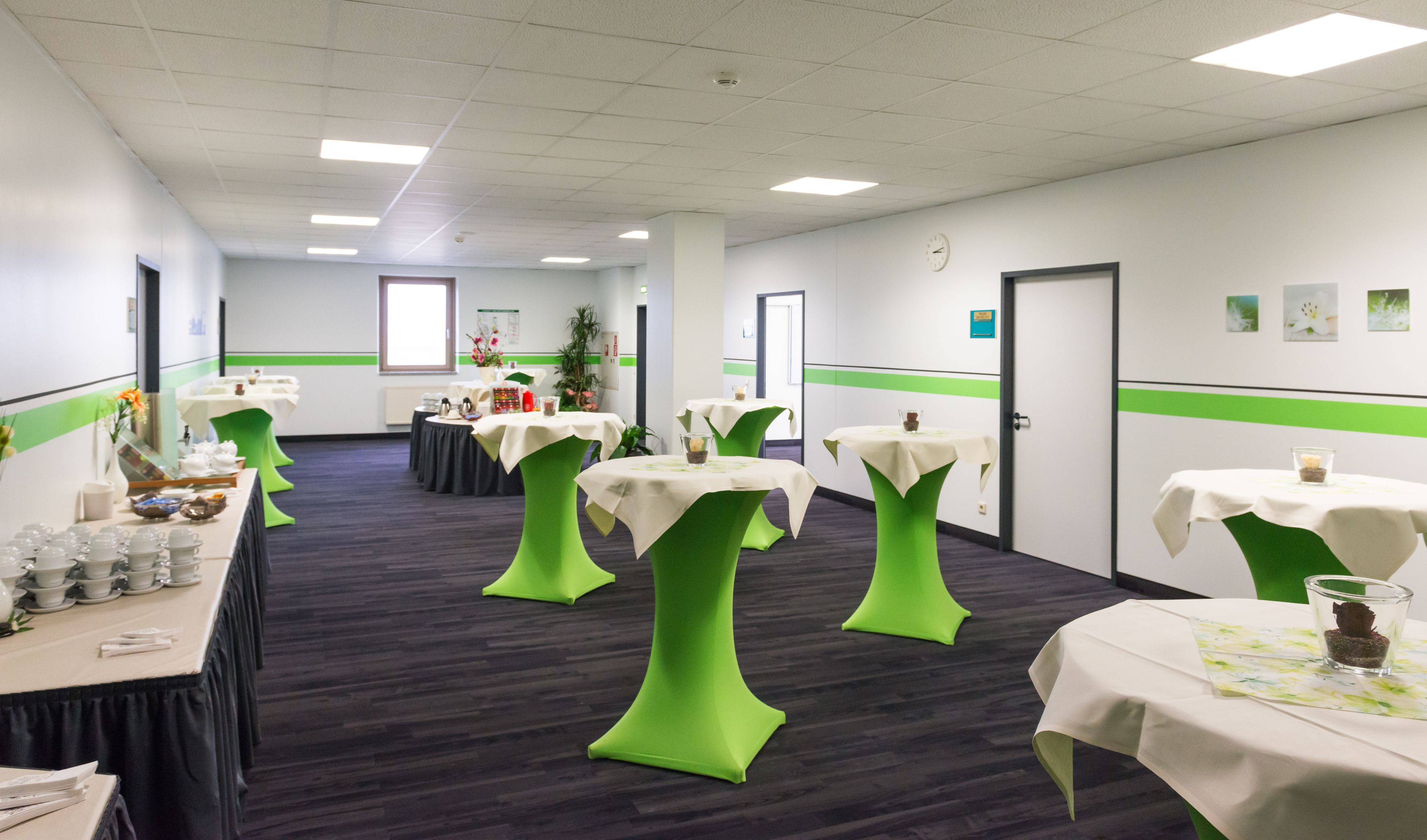 A conference room with multiple tables, green chairs, and a clock on the wall.