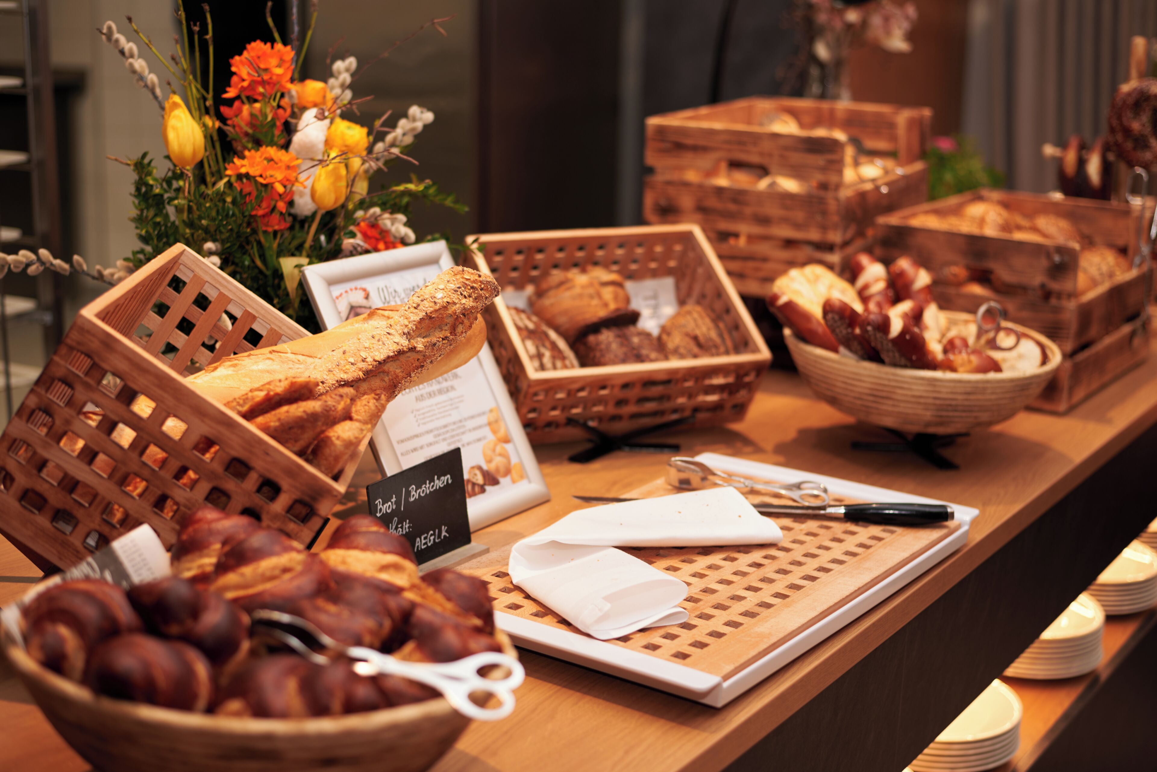 A bakery display with bread and pastries, a sign with menu items, and a decorative flower arrangement.