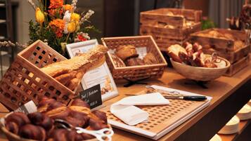 Una vitrina de panadería con pan y pasteles, un letrero con los productos del menú, y un arreglo floral decorativo.