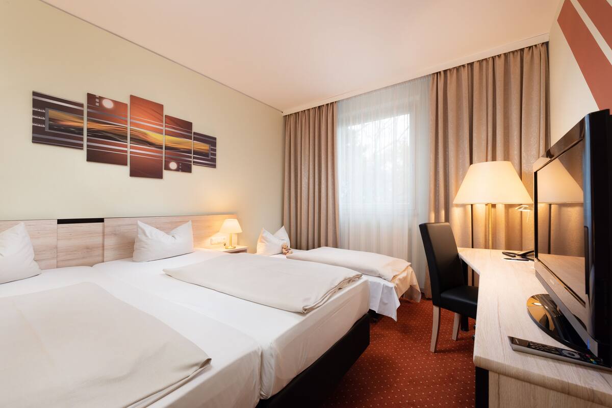 Een hotelkamer met twee bedden, een bureau met stoel, een televisie en een kunstwerk aan de muur.