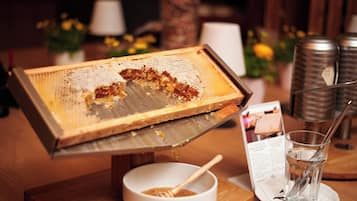 A honeycomb with honeycomb pieces on a tray, a bowl with a honey dipper, and a glass of water on a table.