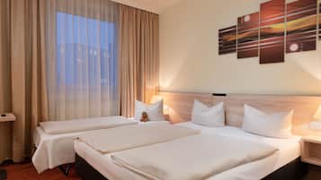 A hotel room with two beds, a large window with sheer curtains, a wall-mounted abstract art piece, and a bedside table with a lamp.