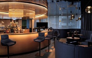 A bar area with a curved counter, multiple stools, and a piano. - NOVINA HOTEL Südwestpark Nürnberg (Nuremberg)