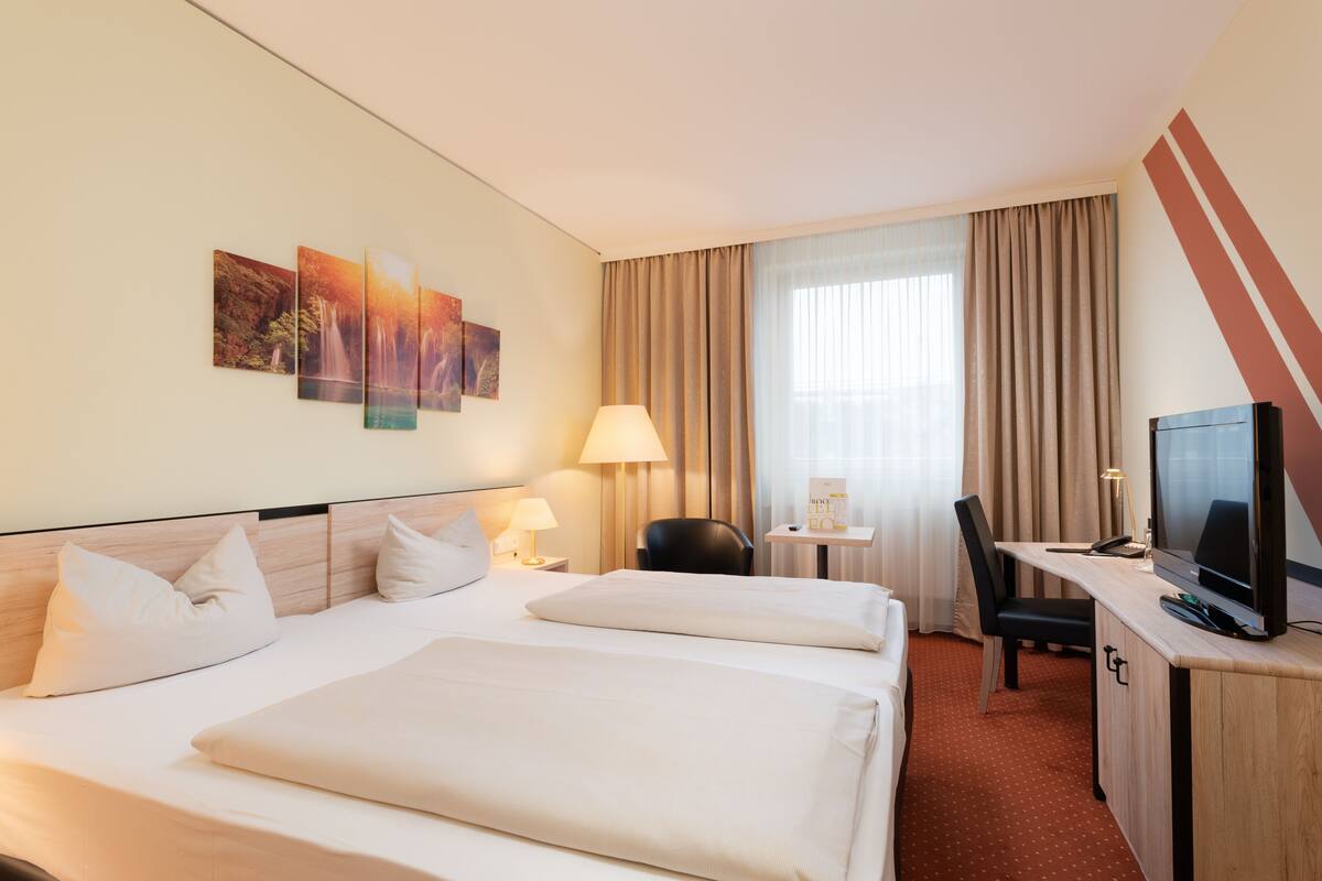 Een hotelkamer met twee bedden, een bureau met een televisie, een stoel, een lamp en kunst aan de muur.