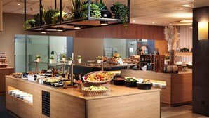 Zona de buffet con diversos alimentos, una estación de café y una exhibición de plantas.