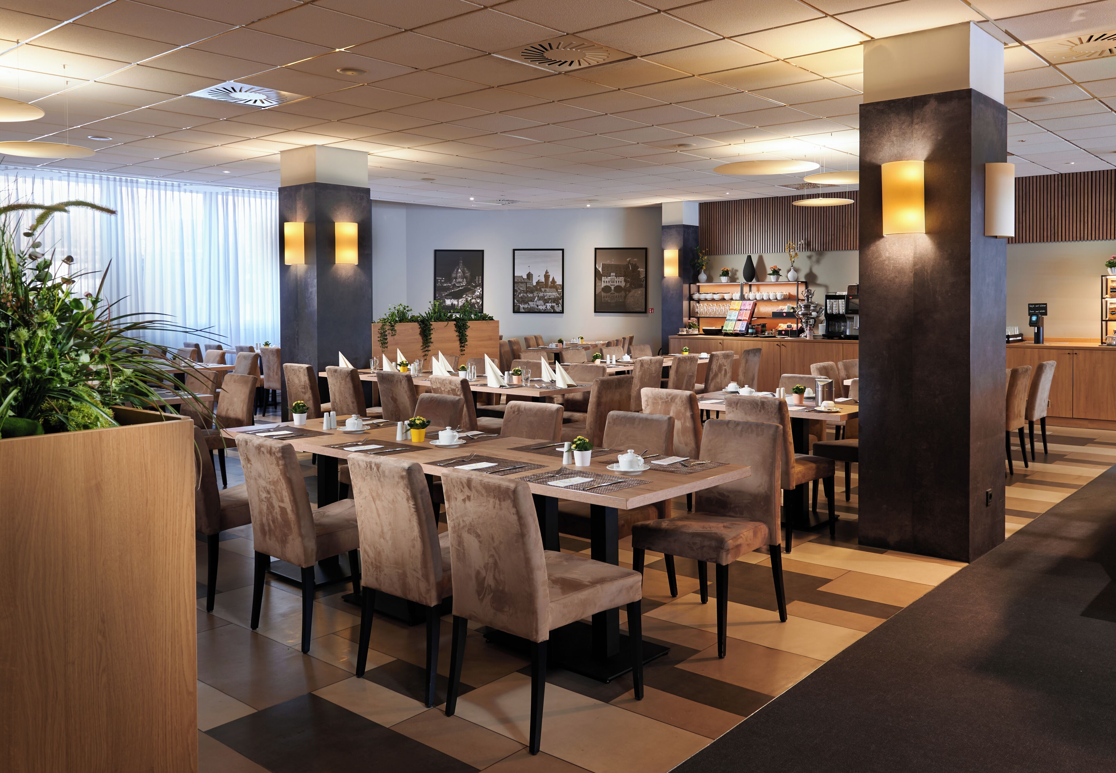 A modern hotel dining area with multiple tables and chairs, a reception desk, and a bar area.