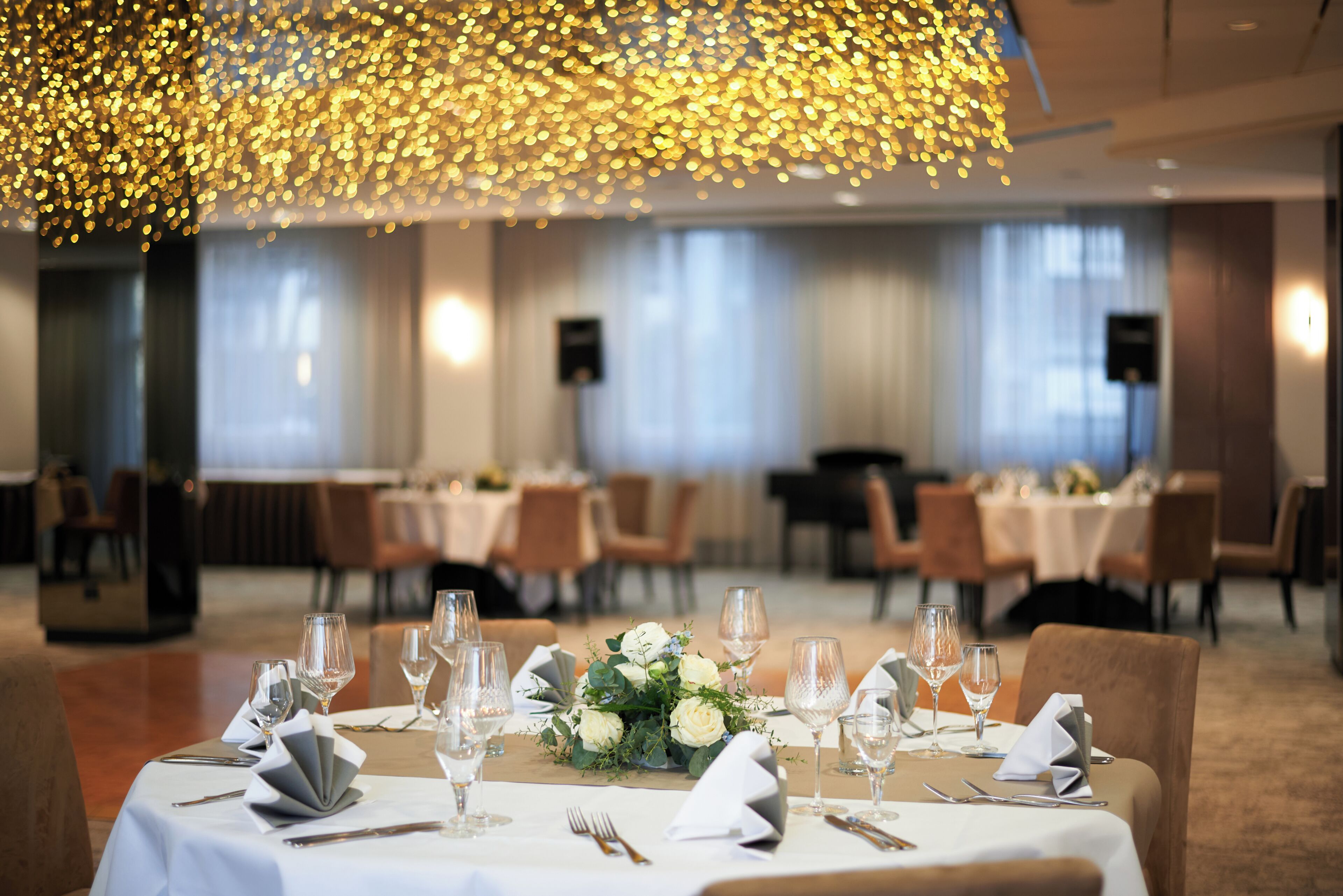 A dining area with tables set for service, a chandelier, and a view of the dining area in the background.