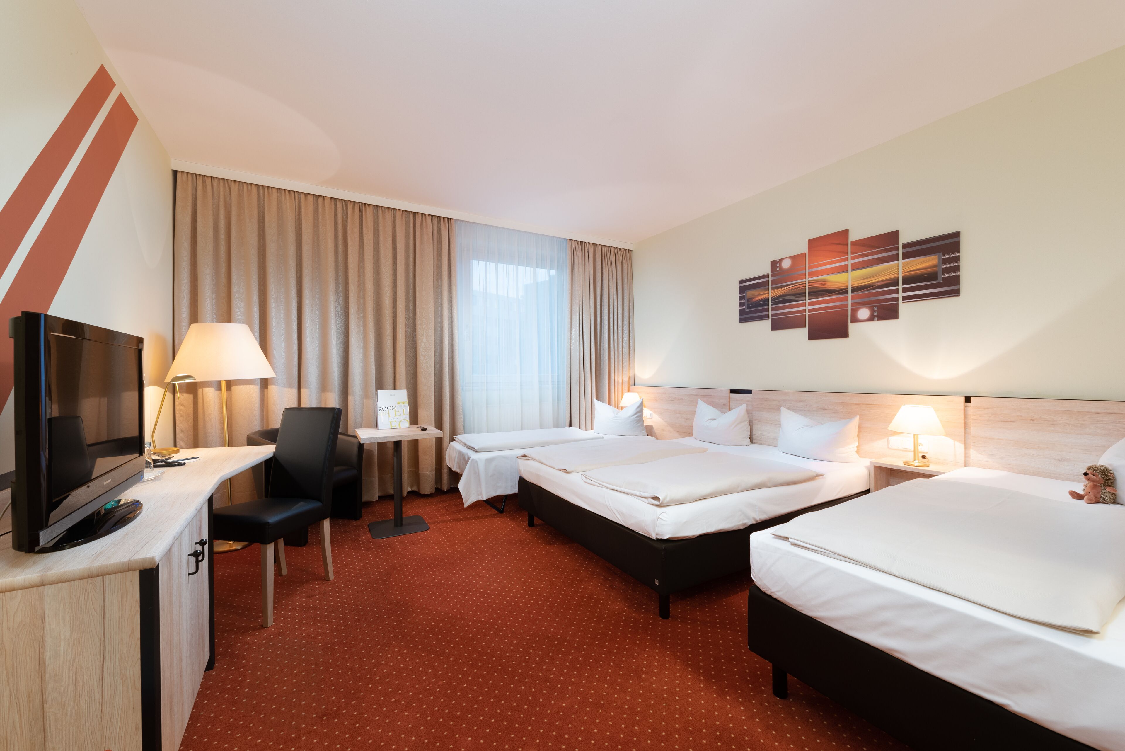 Hotelkamer met twee bedden, een bureau met een televisie, een stoel, een tafeltje en een lamp.