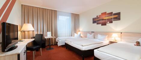 A hotel room with two beds, a desk with a TV, a chair, a small table, and a lamp.