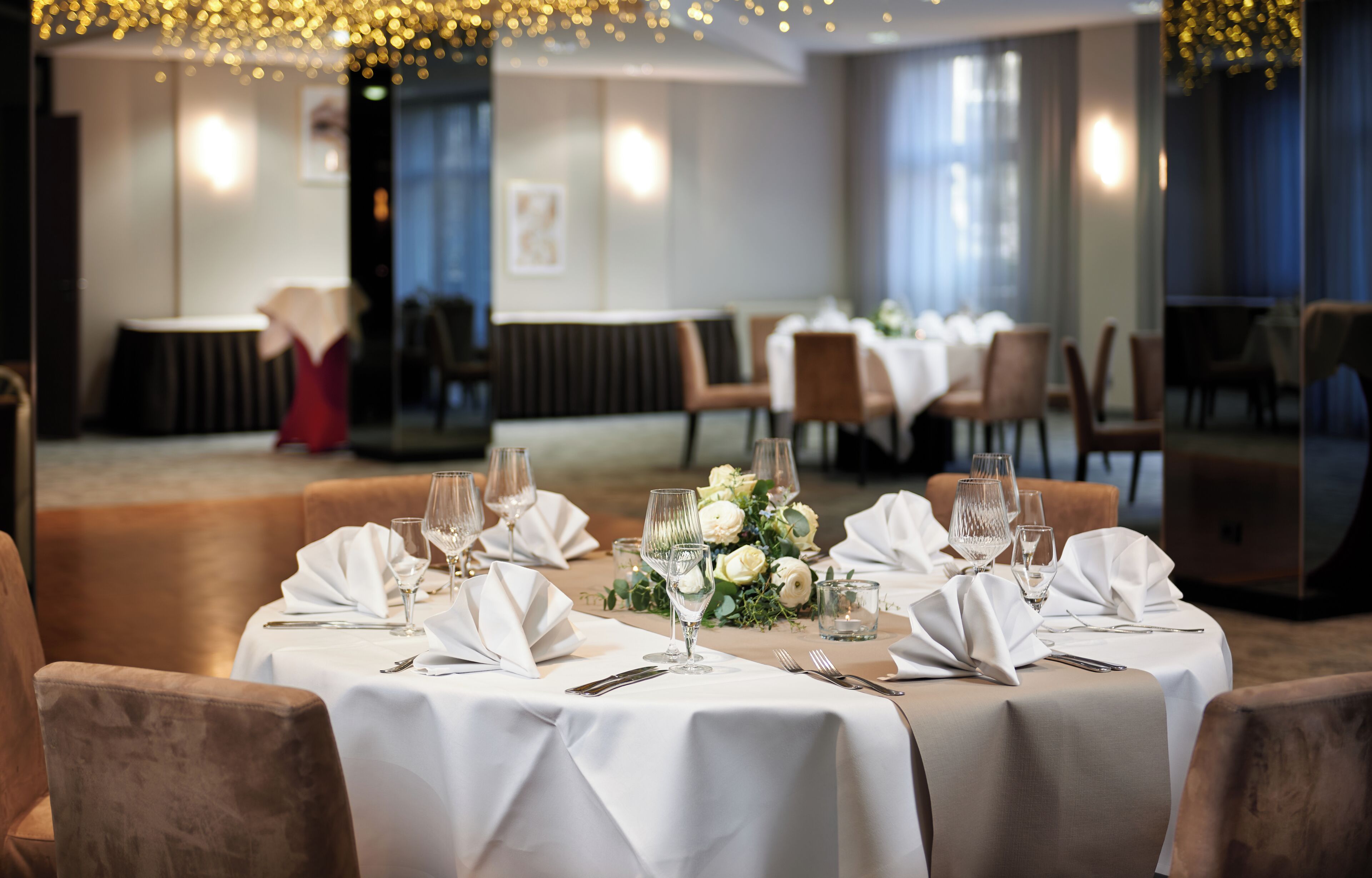 Un restaurant avec des tables rondes dressées pour le dîner, agrémentées de nappes blanches et de beaux verres.