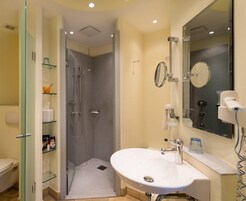 Un baño moderno con cabina de ducha de vidrio, un lavabo blanco con espejo y un secador de pelo sobre la encimera.