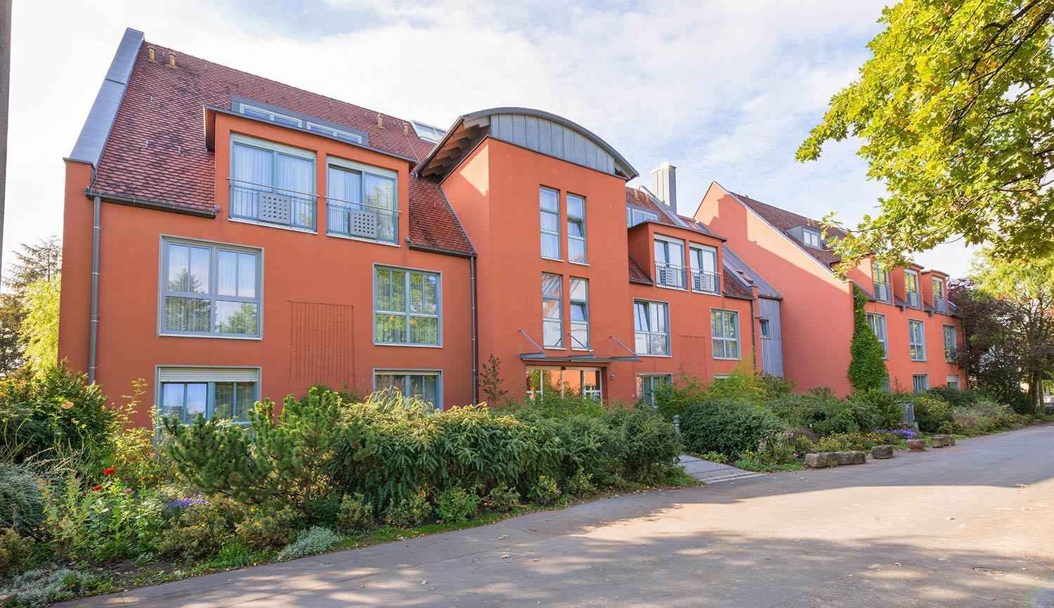 Ein modernes, mehrstöckiges Wohngebäude mit roter Fassade, großen Fenstern und einem gewölbten Dach.