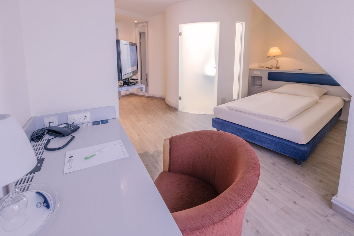 A hotel room with a bed, a desk with a telephone, a chair, and a television.